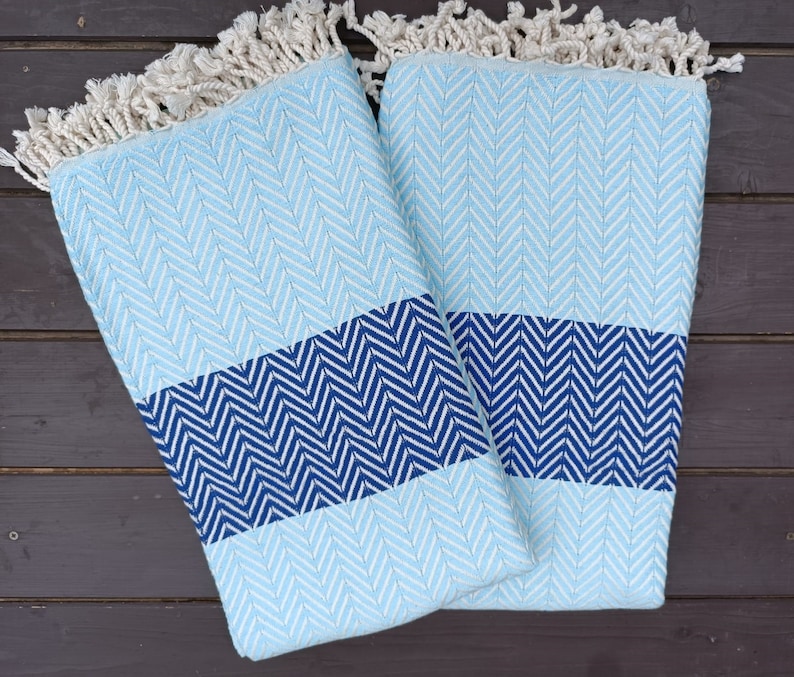 May include: Two blue and white patterned towels with fringe edges. The towels are folded in half and have a chevron pattern.