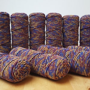 May include: A collection of ten spools of colorful yarn, each spool is a mix of brown, gold, and blue thread. The spools are arranged in two rows on a wooden surface.