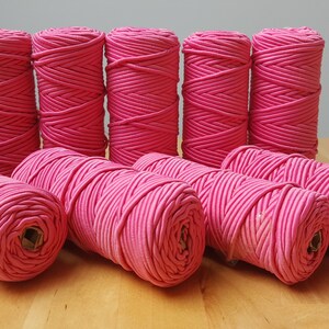 Può includere: Dieci bobine di cordoncino elastico rosa, avvolte strettamente e disposte in due file su una superficie di legno.