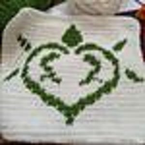 Op de afbeelding: Een witte, rechthoekige decoratieve schaal met een groen hartvormig ontwerp. Het hart is gevuld met een textuurpatroon en twee figuren. Twee pijlen flankeren het hart. De schaal is waarschijnlijk gemaakt van keramiek.
