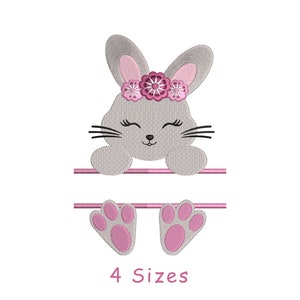 Könnte beinhalten: Stickdatei mit einem grauen Hasen mit rosa Ohren und einer rosa Blütenkrone. Der Hase schaut über eine rosa Leiste mit zwei rosa Pfotenabdrücken darunter. Der Text "4 Größen" befindet sich unter den Pfotenabdrücken.