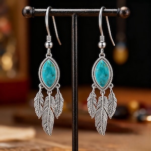 May include: Silver drop earrings with a turquoise oval stone and three feather charms. The earrings are displayed on a black metal stand, highlighting their intricate design and bohemian style.