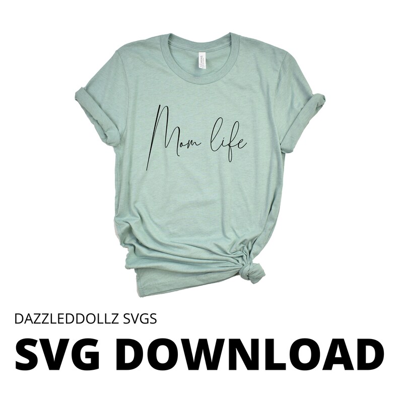 May include: A light green t-shirt with the words "Mom life" in a black script font. The shirt is knotted at the bottom and has rolled-up sleeves. The text "DAZZLEDDOLLZ SVGS" and "SVG DOWNLOAD" are at the bottom of the image.