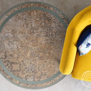 May include: A round rug with a beige and brown floral pattern, framed by a light green border. A yellow armchair with a blue nautical-themed pillow is in the corner. The rug adds a touch of elegance to the room.