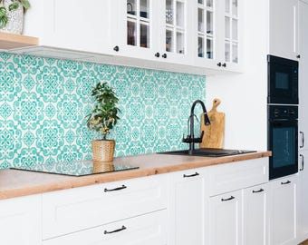 May include: A kitchen featuring white cabinets with glass-paneled doors, a light wood countertop, and a backsplash with a repeating teal and white floral pattern. A black faucet sits by a sink, and a small potted plant rests on the counter.