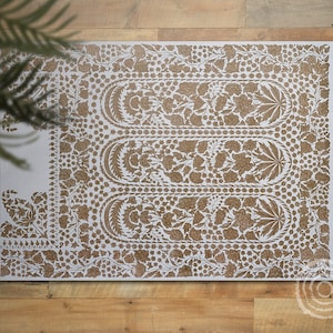 May include: A white rug with a brown floral pattern. The pattern features intricate designs of leaves and flowers.