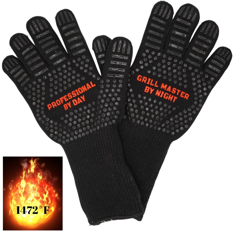 Op de afbeelding: Een paar hittebestendige zwarte handschoenen met een textuur grip. De handschoenen hebben de tekst "Professional by Day" op de ene handschoen en "Grill Master by Night" op de andere. De handschoenen zijn bestand tegen 1472 graden Fahrenheit.