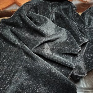 May include: A black velvet fabric with a textured surface. The fabric is folded and draped, showing the soft, plush texture.