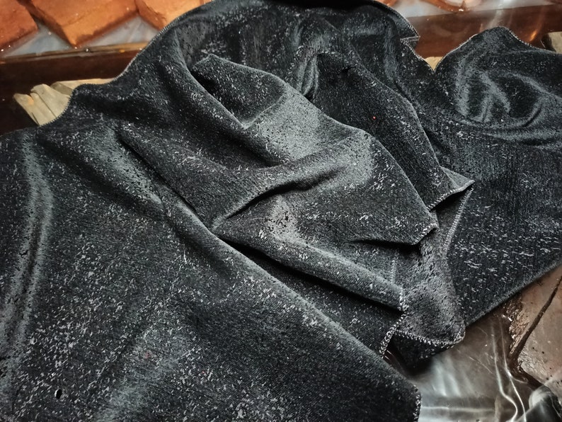 May include: A black velvet fabric with a textured surface. The fabric is folded and draped, showing the soft, plush texture.