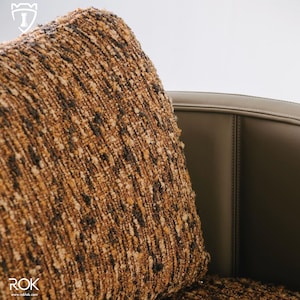 Puede incluir: Primer plano de un coj&iacute;n cuadrado texturizado con un patr&oacute;n moteado marr&oacute;n, beige y negro. El coj&iacute;n se coloca contra una silla de cuero marr&oacute;n oscuro. El conjunto transmite una sensaci&oacute;n de confort y calidad.