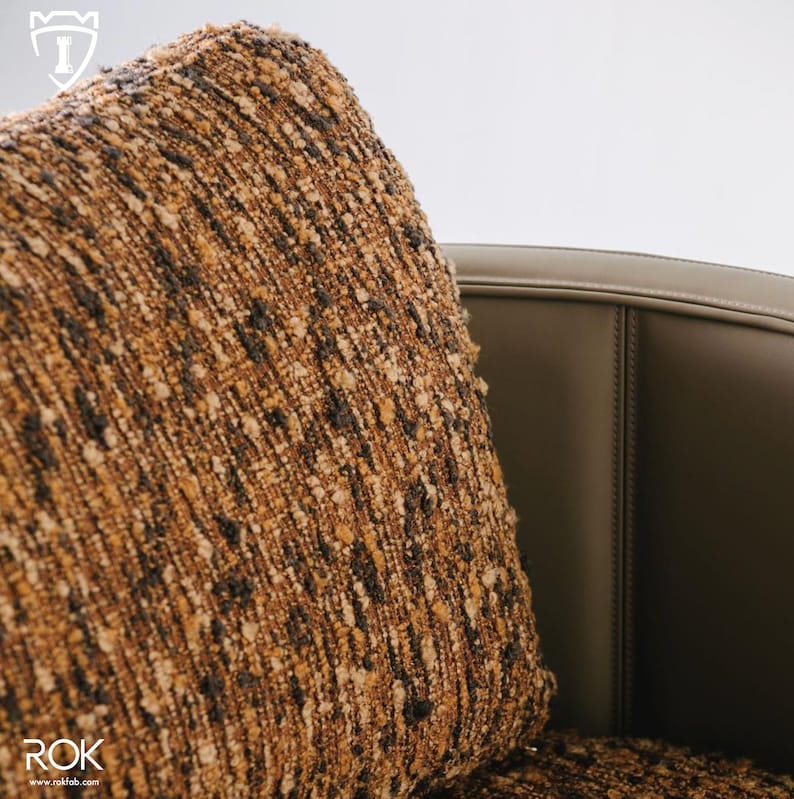 Puede incluir: Primer plano de un coj&iacute;n cuadrado texturizado con un patr&oacute;n moteado marr&oacute;n, beige y negro. El coj&iacute;n se coloca contra una silla de cuero marr&oacute;n oscuro. El conjunto transmite una sensaci&oacute;n de confort y calidad.