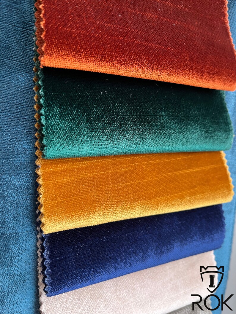 May include: A close-up of five fabric swatches in different colors. The swatches are arranged in a stack, with the top swatch being a rich orange-red, followed by a deep green, a bright yellow, a dark blue, and a light beige.