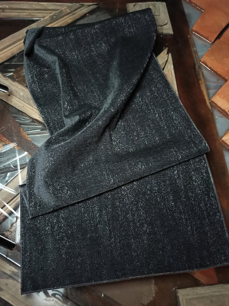 May include: A black fabric with a subtle textured pattern. The fabric is folded in half and has a stitched edge.