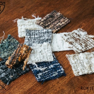 Puede incluir: Una colecci&oacute;n de muestras de tela texturizada en varios colores, incluyendo blanco, azul, marr&oacute;n y gris. Las muestras tienen una apariencia tejida y est&aacute;n dispuestas sobre una superficie de madera. El texto "ROK | E-277" es visible en la esquina inferior derecha.