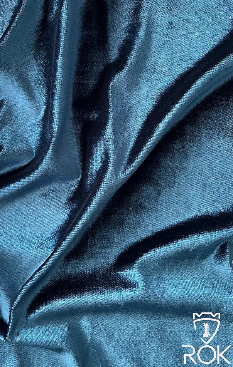 May include: Close-up of a teal blue fabric with a subtle sheen. The fabric is draped and folded, showcasing its texture and drape.