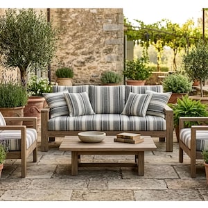 Può includere: Set di mobili da giardino con divano a righe, due poltrone e un tavolino in legno. I cuscini presentano un motivo a righe grigie e bianche. La scena è ambientata in un giardino con piante e alberi in vaso.