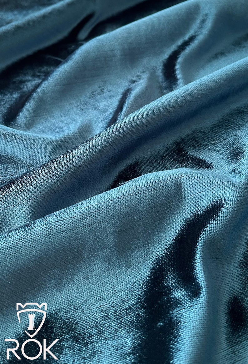 May include: Close-up of a teal blue velvet fabric with a subtle sheen. The fabric is soft and luxurious, with a slightly textured surface.
