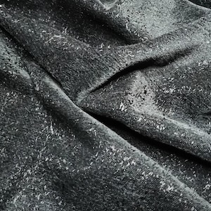May include: Close-up of a dark gray fabric with a textured, speckled pattern. The fabric is folded and wrinkled, creating a dramatic and abstract look.
