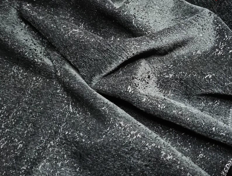 May include: Close-up of a dark gray fabric with a textured, speckled pattern. The fabric is folded and wrinkled, creating a dramatic and abstract look.