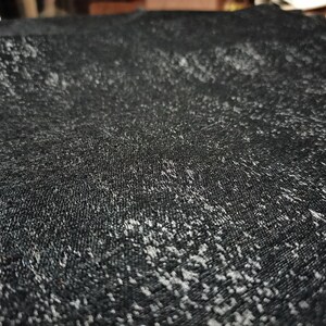 May include: Close-up of a black fabric with a subtle shimmery texture. The fabric has a slightly rough, textured surface.