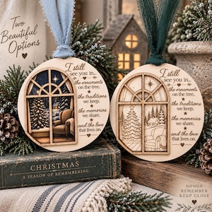 May include: Two round wooden Christmas ornaments featuring a laser-cut window design. One ornament displays a coloured winter scene, while the other shows a natural wood engraving. Both include the text: I still see you in the ornaments on the tree, the traditions we keep, the memories we share, and the love that lives on.