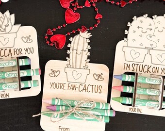 Puede incluir: Cuatro tarjetas de madera para el Día de San Valentín con diseños de cactus y suculentas. Cada tarjeta tiene un mensaje ingenioso y un juego de crayones. Los mensajes son "Aloe You Very Much", "I'm a Succa for You", "You're Fan-Cactus", y "I'm Stuck on You".