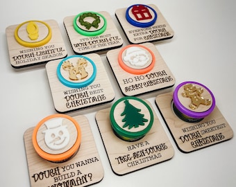 May include: A collection of wooden dough stampers with various Christmas-themed designs, including a snowman, Christmas tree, and gingerbread man. Each stamper has a colorful border and a festive message, perfect for holiday baking.