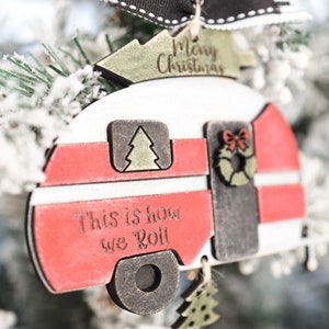 May include: A red and white wooden camper ornament with the text "This is how we roll" and "Merry Christmas". The ornament has a black and white striped bow and a red bead.