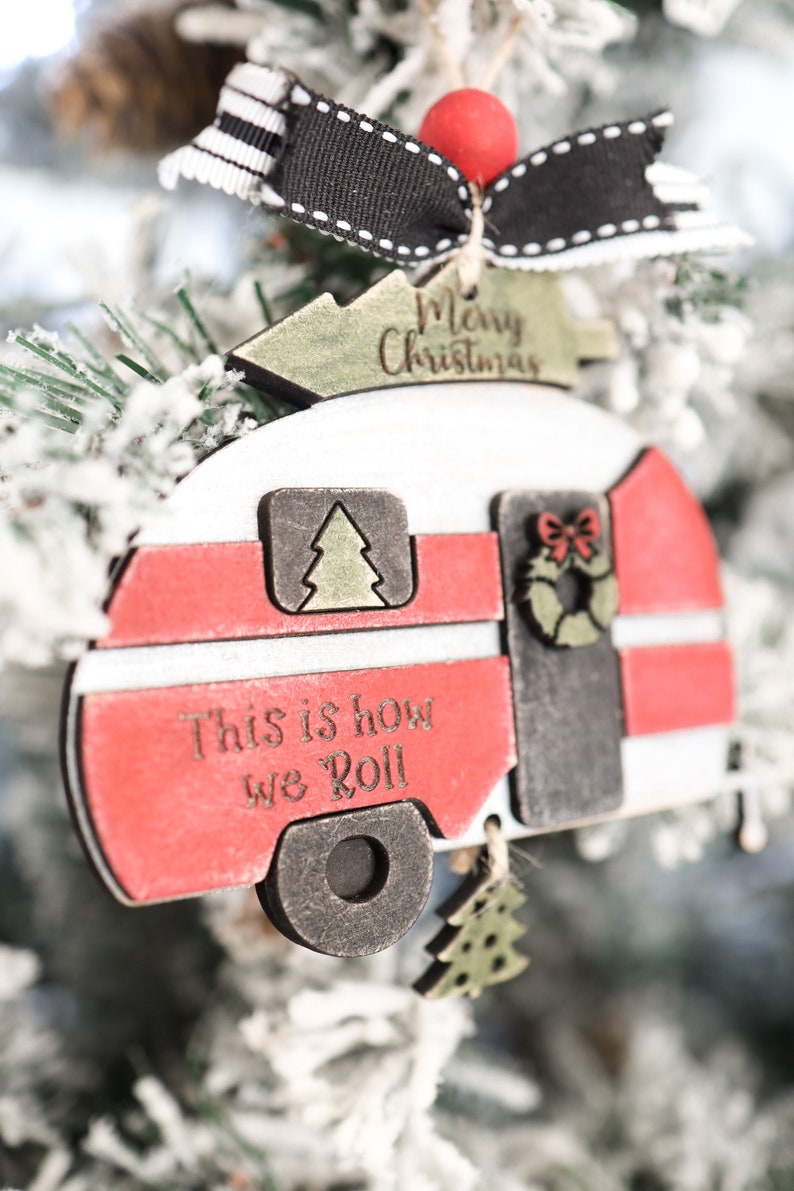 May include: A red and white wooden camper ornament with the text "This is how we roll" and "Merry Christmas". The ornament has a black and white striped bow and a red bead.