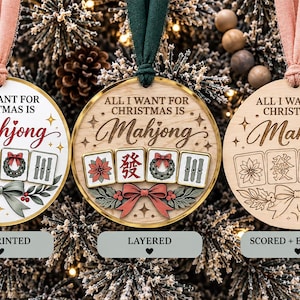 May include: Three round Christmas ornaments with pink and green ribbons. Each features the text "ALL I WANT FOR CHRISTMAS IS Mahjong" and an illustration of four mahjong tiles, a bow, and holly. The ornaments are UV printed, layered, or scored.