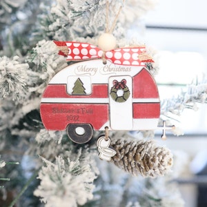 May include: A red and white wooden camper Christmas ornament with the text "Merry Christmas" and "Summer's Fun 2022". The ornament has a red and white polka dot ribbon and a small wooden toilet charm.