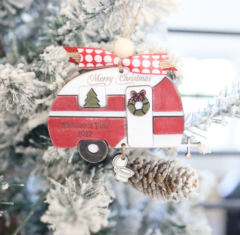 May include: A red and white wooden camper Christmas ornament with the text "Merry Christmas" and "Summer's Fun 2022". The ornament has a red and white polka dot ribbon and a small wooden toilet charm.
