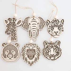 May include: Six wooden ornaments featuring different animal faces, including a giraffe, elephant, jaguar, panda, lion, and tiger. Each ornament is laser-cut with intricate details and has a small wooden bead for hanging.