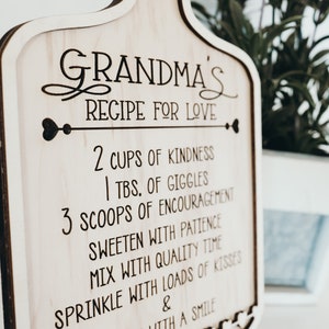 May include: A wooden cutting board with a recipe for love engraved on it. The recipe includes 2 cups of kindness, 1 tablespoon of giggles, 3 scoops of encouragement, sweeten with patience, mix with quality time, sprinkle with loads of kisses, and serve with a smile.