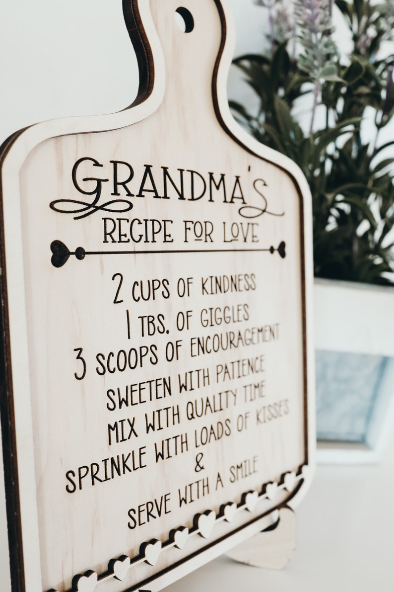 May include: A wooden cutting board with a recipe for love engraved on it. The recipe includes 2 cups of kindness, 1 tablespoon of giggles, 3 scoops of encouragement, sweeten with patience, mix with quality time, sprinkle with loads of kisses, and serve with a smile.
