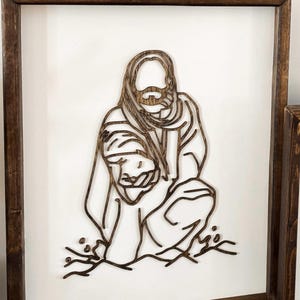 Puede incluir: Una pieza de arte de pared enmarcada en madera con un dise&ntilde;o de corte l&aacute;ser de una persona sosteniendo a un ni&ntilde;o. El dise&ntilde;o es de color marr&oacute;n oscuro y se coloca sobre un fondo blanco.