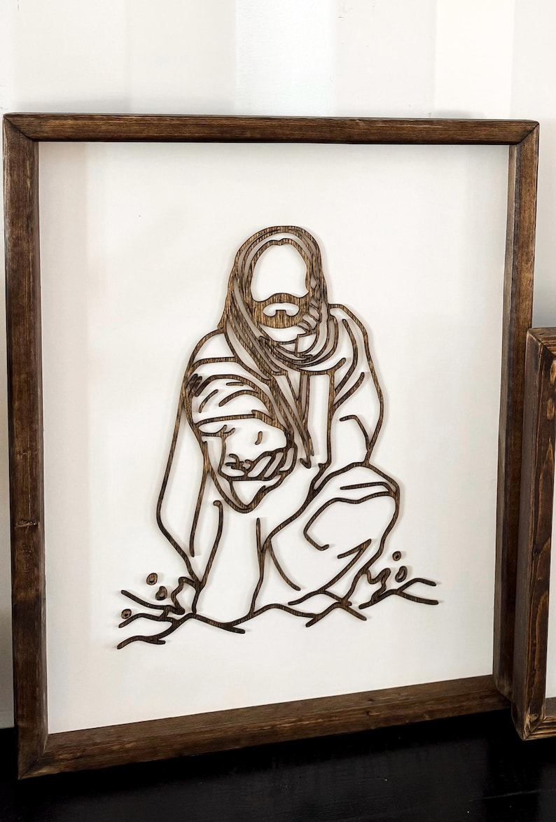 Puede incluir: Una pieza de arte de pared enmarcada en madera con un dise&ntilde;o de corte l&aacute;ser de una persona sosteniendo a un ni&ntilde;o. El dise&ntilde;o es de color marr&oacute;n oscuro y se coloca sobre un fondo blanco.