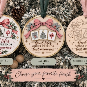 May include: Three round wooden ornaments with pink or green ribbons. Each features a bow, three mahjong tiles with holiday designs, and the text Good tiles GREAT FRIENDS best memories. The finishes include UV printed, layered, and scored and engraved.