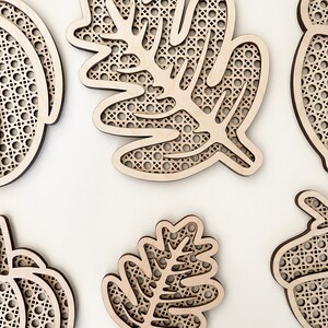 May include: Five wooden cutouts of leaves and pumpkins with a woven pattern. The cutouts are unfinished and ready to be painted or stained.