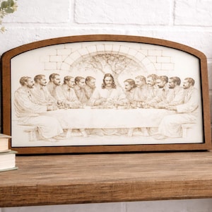 May include: A framed artwork depicting the Last Supper. The image features a detailed sepia-toned illustration of Jesus and his disciples seated at a table. The frame is a dark brown with an arched top.