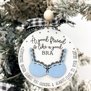 May include: A white round ornament with a blue bra design and the text "A good friend is like a good BRA + SUPPORTIVE. NEVER LEAVES YOU HANGING. & ALWAYS CLOSE TO YOUR HEART +"
