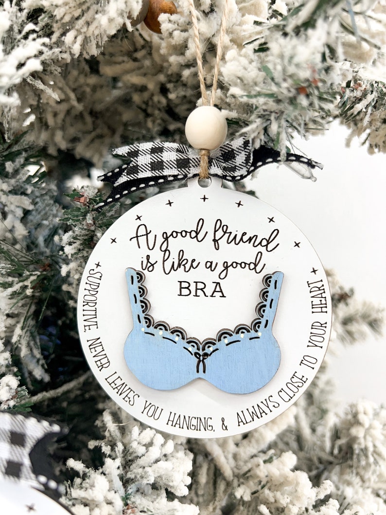 May include: A white round ornament with a blue bra design and the text "A good friend is like a good BRA + SUPPORTIVE. NEVER LEAVES YOU HANGING. & ALWAYS CLOSE TO YOUR HEART +"