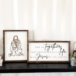 Puede incluir: Dos letreros de madera con fondo blanco y texto negro. El primer letrero presenta un dibujo lineal de una persona con un ni&ntilde;o. El segundo letrero dice "AND SO TOGETHER THEY PRAYED & BUILT A LIFE WITH JESUS AT ITS CENTER".