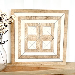 May include: A square wooden wall decor with a geometric pattern of white and brown squares and lines. The decor has a light wood frame.