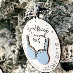 May include: A white wooden ornament with a blue bra cutout and the text "A good friend is like a good bra supportive never leaves you hanging & always close to your heart".