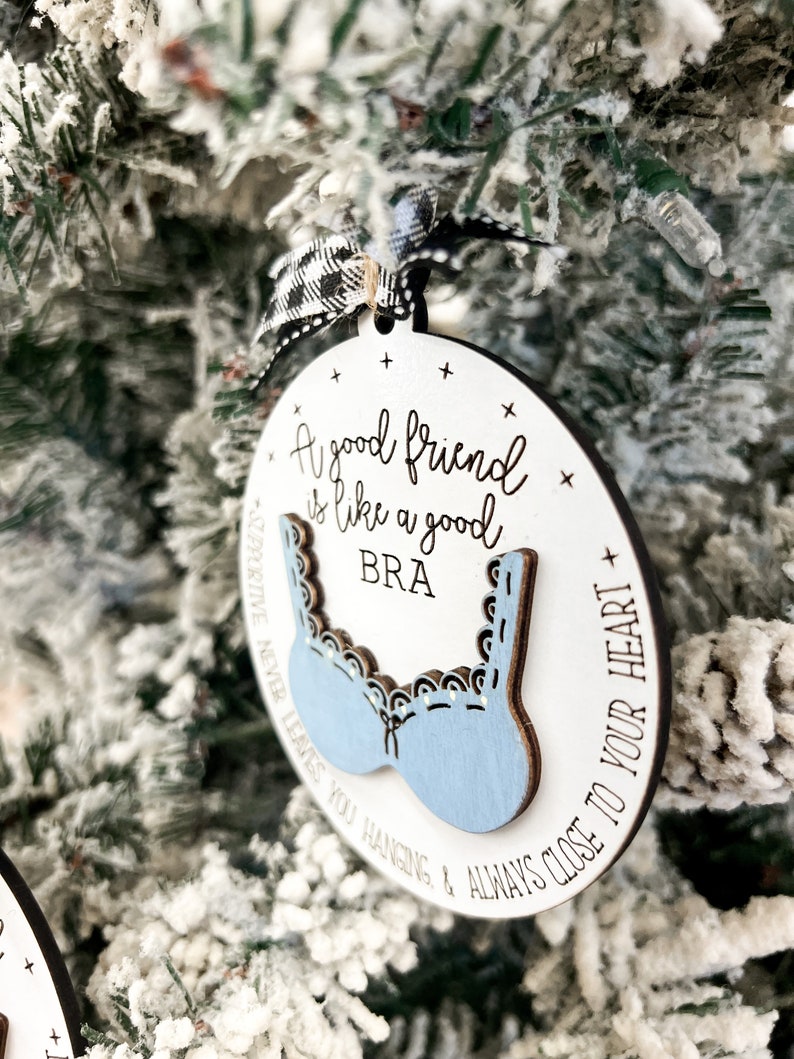 May include: A white wooden ornament with a blue bra cutout and the text "A good friend is like a good bra supportive never leaves you hanging & always close to your heart".
