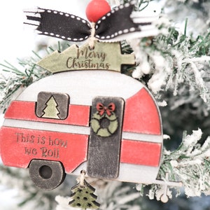 May include: A wooden Christmas ornament shaped like a camper with the text "Merry Christmas" and "This is how we roll". The camper is red, white, and black with a green Christmas tree on top.