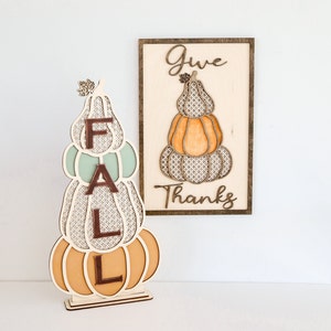 May include: Wooden autumn decor with a stack of pumpkins spelling out "FALL" and a sign that says "Give Thanks".