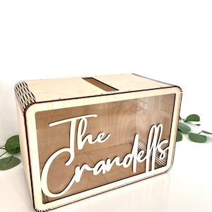 May include: A wooden box with a clear acrylic front panel. The box has a slot on the top for inserting cards or envelopes. The text "The Crandells" is cut out of the front panel.