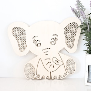 May include: A white wooden elephant cutout with a woven pattern on the ears, trunk, and feet. The elephant has large eyes and a small trunk.